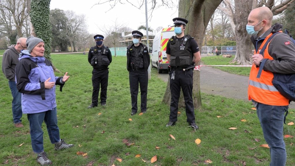 Woman talking to three police officers and a man in an orange work vest, wearing facemasks